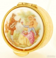 YBM & porcelain pill box, multi-colored image of a woman picking flowers and a man playing a guitar